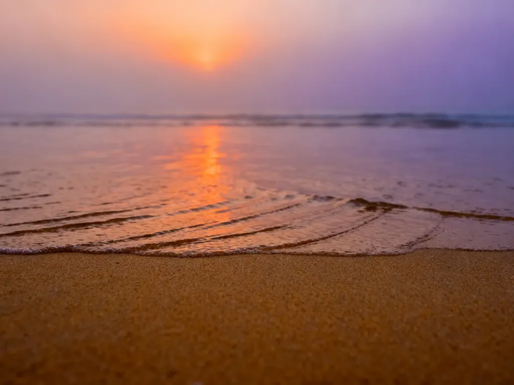 Złocista plaża w Jantarze o wschodzie słońca z malowniczymi refleksami światła na spokojnej tafli Bałtyku.